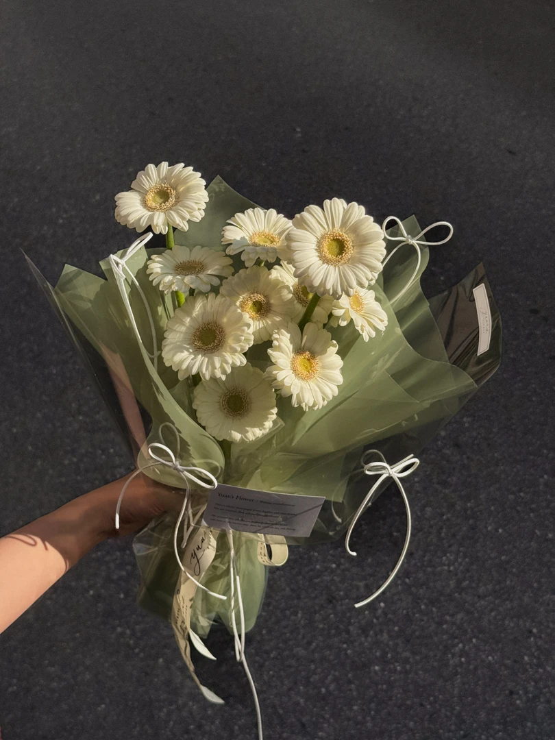 奶油白非洲菊花束包裝細節，綠色果凍玻璃紙與白色韓國麂皮緞帶