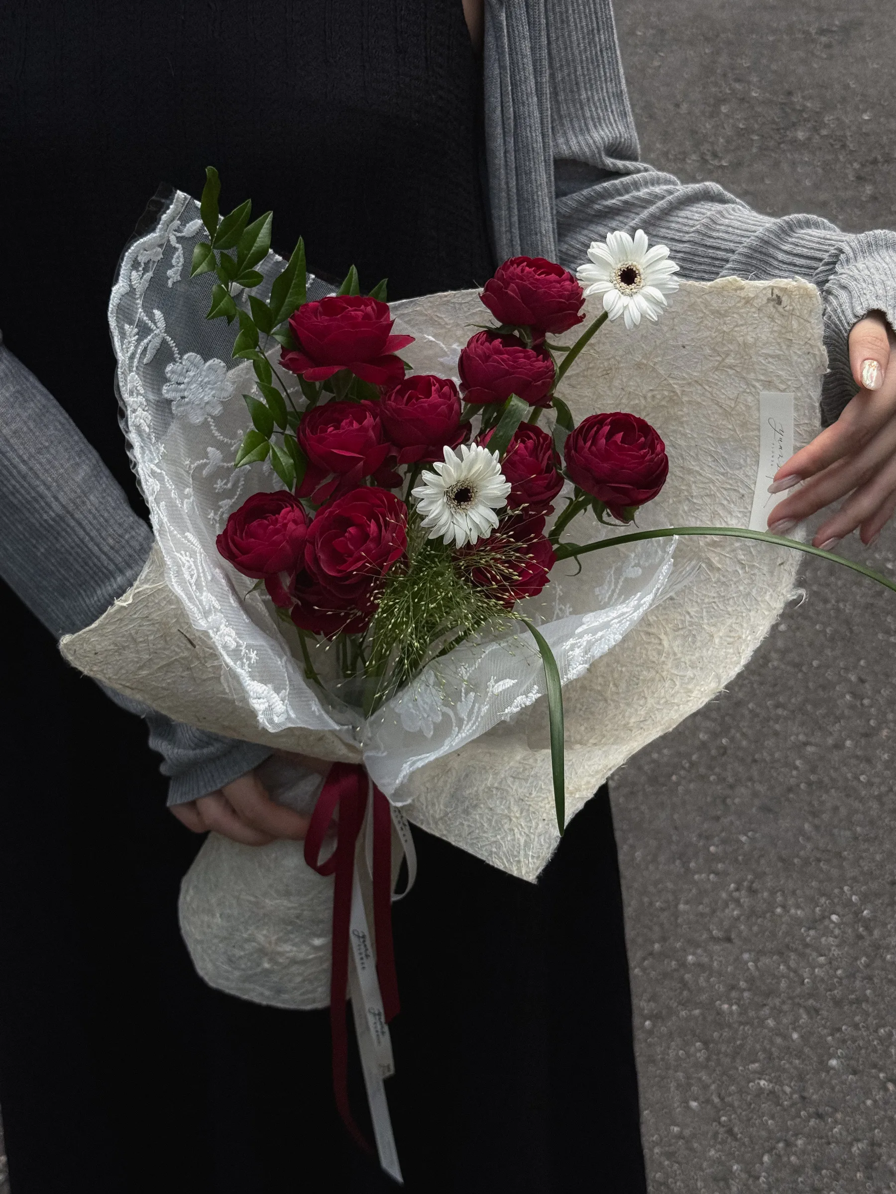 女生手持紅蕾絲泡泡玫瑰花束，酒紅球型玫瑰，米白手工紙與白色蕾絲包裝